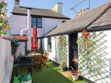 An outdoor patio with a wooden table and chairs a closed red umbrella artificial grass and wall trellises with flowers at The Funky Flat in Holywell