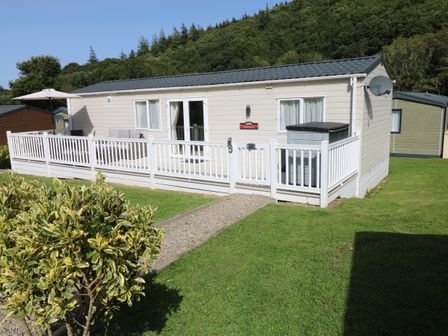 A beige mobile home with a white fence and patio area on a grassy plot at 116 Woodpecker Lodge in Gilfachrheda near Llanarth