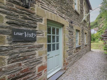 A stone house with a green door and windows and a sign reading Lower Vestry at Lower Vestry in Llangrannog