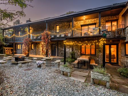 An outdoor patio area with string lights stone benches a fire pit and a wooden table at The Waterfall Retreat in Orton