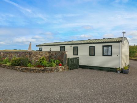 A mobile home with a tiled roof next to a stone wall and garden at Cae Gog Near Cemaes Bay