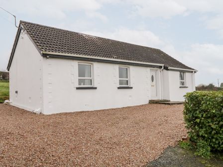 A white single-story house with a tiled roof and three windows on a gravel driveway at Rose Cottage in Omagh