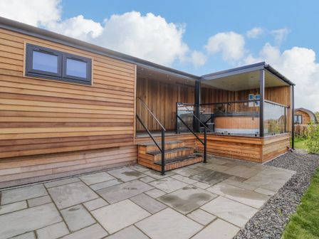 An exterior view of a wooden lodge with steps leading to a covered porch with glass railings at Betsi Lodge 1 in Llanelidan near Corwen