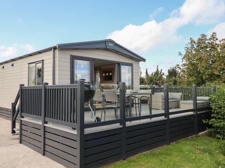 A modern mobile home with an outdoor deck furnished with a dining table chairs a grill and seating at Hazel Lodge in Teigngrace near Newton Abbot