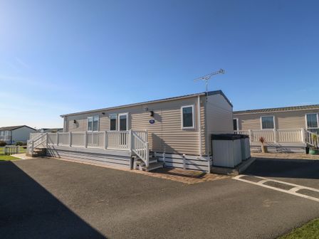 A static caravan with a white railing and steps on a paved area at Seafront Holiday Home 2 in Pwllheli