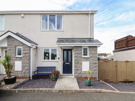The front exterior of a two story house with a blue door a blue bench potted plants and wooden fence at Tritons Retreat in Moelfre