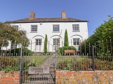 White two story house with gated front garden and wooden bench at Charmouth Lodge in Charmouth