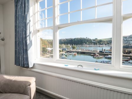 Window with a view of a harbor with boats and hills inside a room with blue curtains and a beige sofa at Quayside in Dartmouth