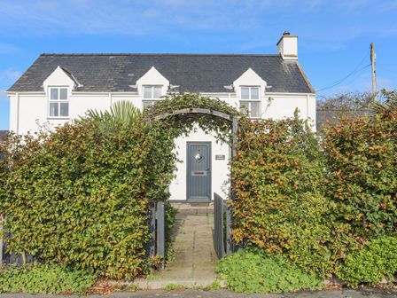 A white two-story house with a arched plant-covered gateway and green front door at Bron Gadair in Mynytho near Llanbedrog
