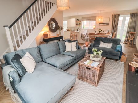 A living room with sofas and a wicker coffee table near a dining area at Driftwood Sands in Beadnell