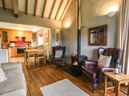 A living room with two armchairs a wood stove and a dining table near a kitchen at The Old Dairy Whitchurch Canonicorum near Charmouth
