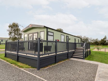 A light green caravan with a black wooden deck and steps outside surrounded by gravel and grass at Silverdale View in East Heslerton near Sherburn