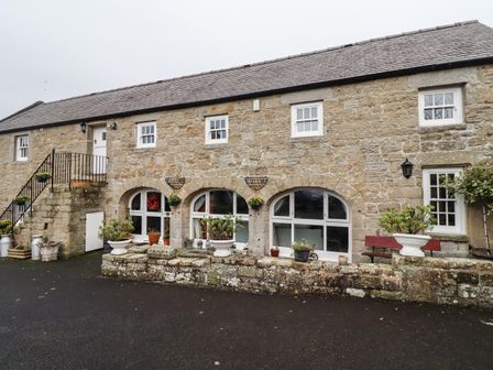 The exterior of a stone building with arched ground floor windows and stairs leading to a white door at High Shaftoe in Ponteland