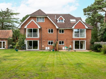 A large brick house with multiple windows and balconies overlooking a lawn with outdoor seating at The Gables Penthouse in Bournemouth