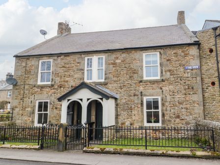 A stone house with white framed windows and black metal fence at Tyne View Cottage in Bellingham
