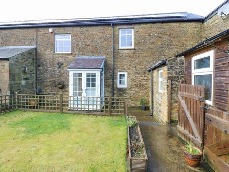 A stone house with white windows and doors with a small fenced garden area at The Byre in Carrshield near Allendale