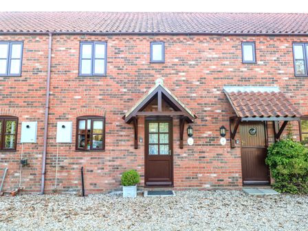 A brick house exterior with two brown doors and four windows at Brimstone in East Ruston near Stalham