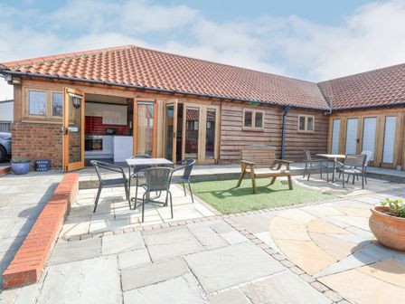An outdoor patio area with tables and chairs a wooden bench and a tiled floor at 5a Hideaways in Hunstanton