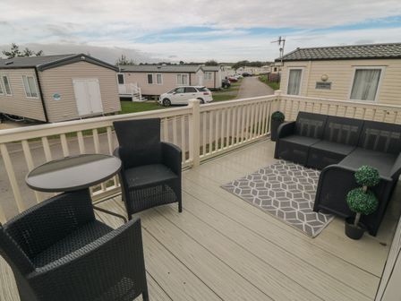 An outdoor deck with black wicker furniture including chairs a table and a sofa with a patterned rug and potted plants at No30 Elm Rise in Gristhorpe near Filey