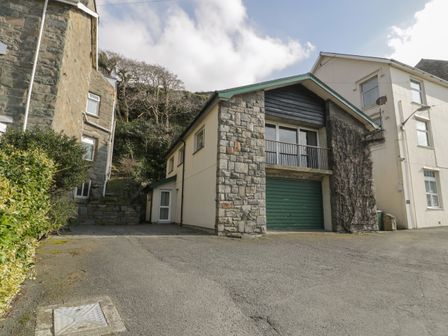 A driveway leading to a two-story house with stone and cream exterior walls and a green garage door at Borthwen in Barmouth