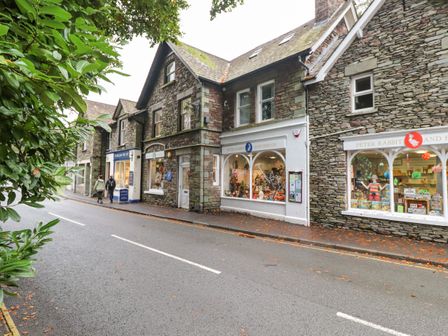 A stone building with shops and pedestrians on a street with trees on the side at Riverbank in Grasmere