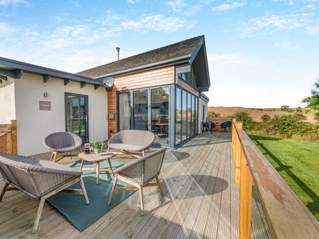 An outdoor wooden deck with wicker chairs and a table at Shearwater Lodge in Bamburgh