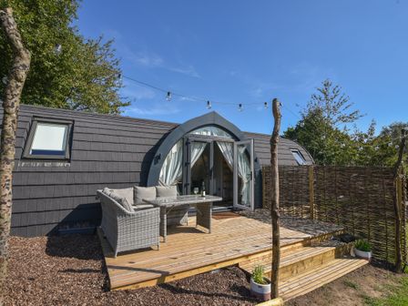 An outdoor wooden deck with seating and table in front of a pod-style building with string lights and trees at Maple in Wootton Fitzpaine near Charmouth