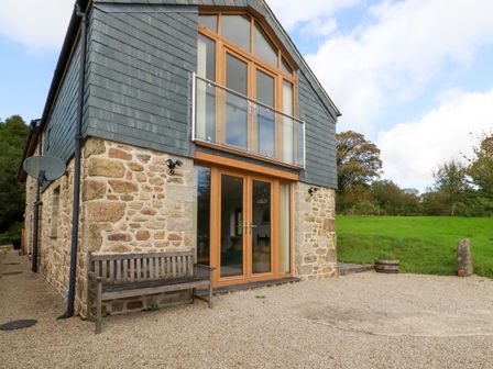 Exterior view of a stone and wood house with a bench and gravel area in front at The Orchard in Cardinham