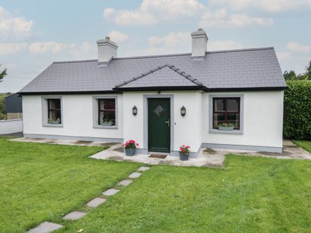 A single story house with a dark green front door two chimneys and a lawn with stepping stones at Kates Cottage Killawullaun near Ballintubber County Mayo