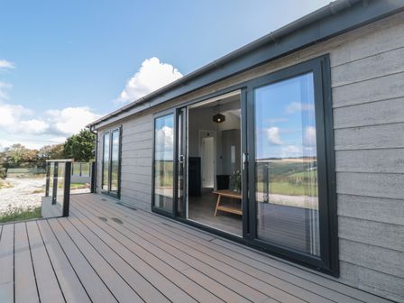 A terrace with glass railing and sliding doors leading to a room at Buttercup Lodge in Norton near Dartmouth