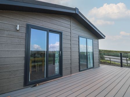An exterior deck with sliding glass doors overlooking a railing and landscape at Honeysuckle Lodge in Norton near Dartmouth