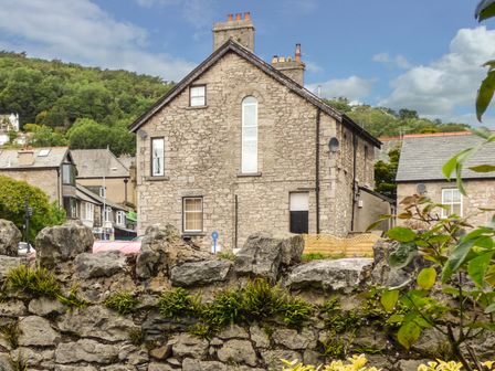 A stone house with a stone wall in front and trees in the background at Church View in Grange-Over-Sands