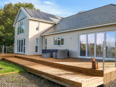 A two story house with solar panels on the roof and a wooden deck with outdoor furniture and a dog sitting on the deck at Linden View in Combe Martin