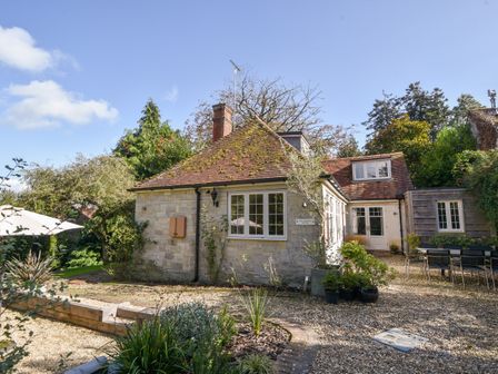 A stone and wood house with gravel driveway and outdoor dining area at The Carriage House in Uplyme