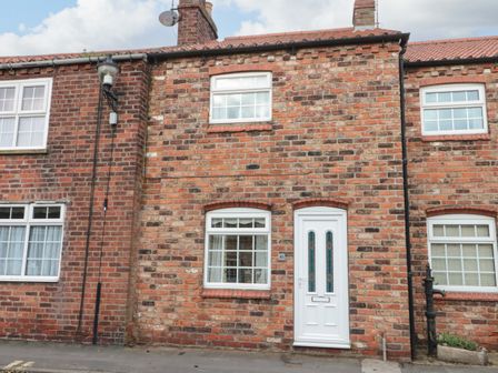 Brick terraced house with white framed windows and a white door on a street at Shell Seeker Cottage in Sewerby