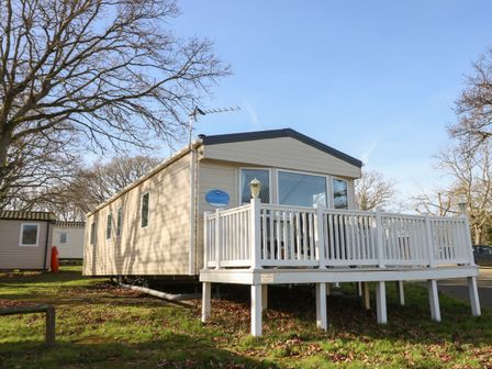 A static caravan with a white wooden deck surrounded by trees at 15 Rosewood Great Thorness near Northwood Isle Of Wight
