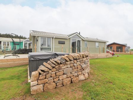 A mobile home with a stone wall and a hot tub on a grassy area at No.7 Skiddaw View in Moota near Aspatria