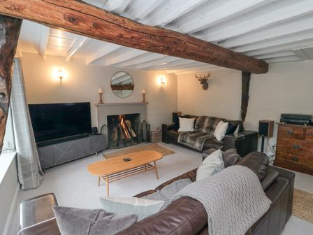 A living room with two leather sofas a wooden coffee table a fireplace with a fire a large TV and exposed wooden ceiling beams at York House in Thornton Dale