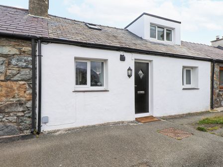 A white cottage with a black door and two windows on either side at Quarry Cottage in Bethesda