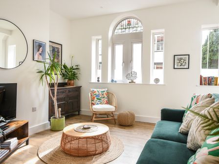 A living room with a green sofa round wicker coffee table wooden sideboard and two plants at Seaward in Lyme Regis