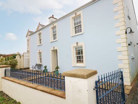 The exterior of a two-story light blue house with white trim and a blue metal gate at The Old Boathouse in Trefin near St Davids