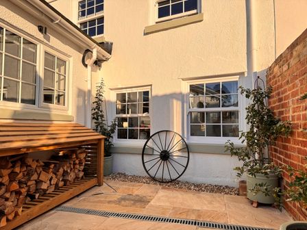 A courtyard with stacked firewood a metal wheel and potted plants at Pilchard Cottage in Dawlish