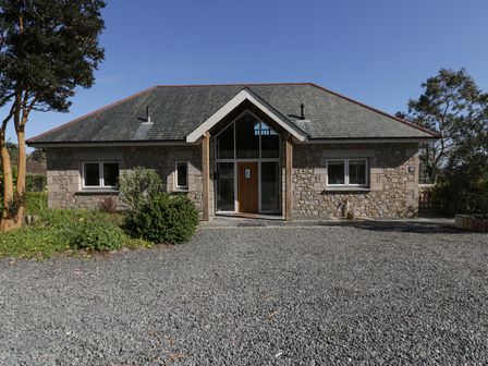 A stone house with a pitched roof a wooden front door surrounded by glass and a gravel driveway at Lower Mellan Barn in Coverack