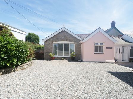 A gravel driveway in front of a stone and pink painted house with plants in pots at Bwthyn Yr Hafod in Benllech