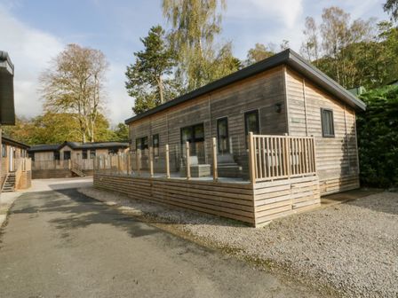 A wooden cabin with a deck and glass railing surrounded by trees at The Bothy in Keswick
