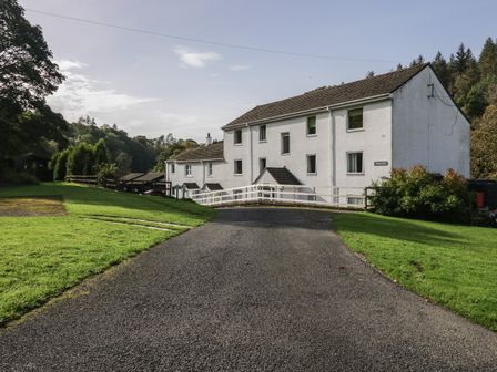 A white multi-story building with several windows at the end of a paved driveway surrounded by grass and trees at Apartment 4 in Keswick