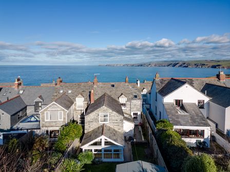 A row of houses with slate roofs facing the sea and cliffs in the background at Tre Lowen in Port Isaac