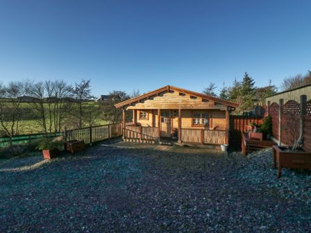 A wooden cabin with a fenced yard and planters in a rural area at Ballinorig Lodge in Cleator Moor