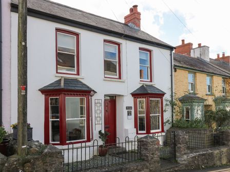 A white two-story house with red window frames and a red door with a small front garden at Ty Len in St Davids