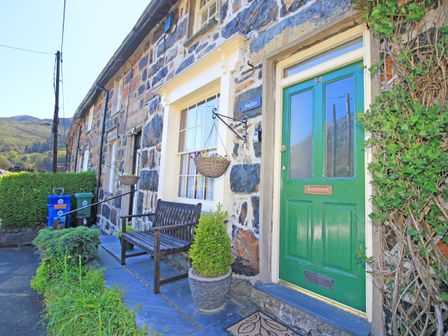 Stone house exterior with a green door a wooden bench hanging flower basket and potted plant at Hafan Cottage in Beddgelert